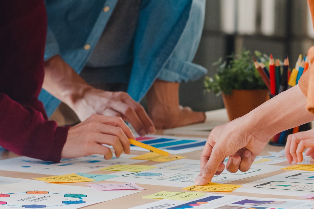 Asian businessmen and businesswomen meeting brainstorming ideas about creative web design planning application and developing template layout for mobile phone project working together in small office.